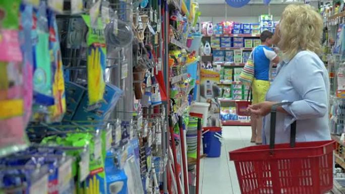 高级妇女正在超市中选择带有购物篮的家用物品进行清洁