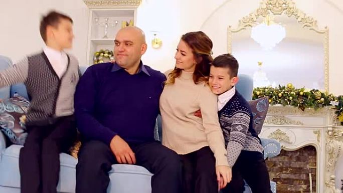 模范家庭，充满爱心的父母和儿子的肖像，他们坐在节日装饰的房间里的蓝色沙发上，下午有圣诞树和壁炉
