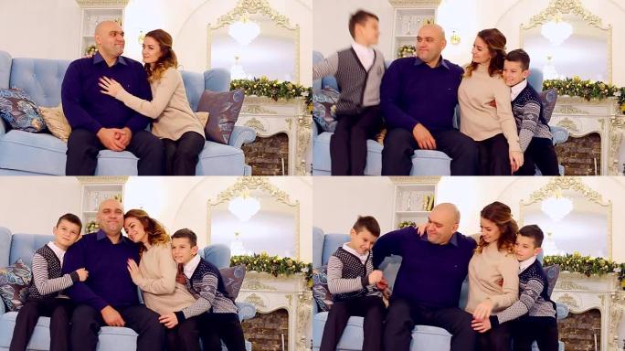 模范家庭，充满爱心的父母和儿子的肖像，他们坐在节日装饰的房间里的蓝色沙发上，下午有圣诞树和壁炉