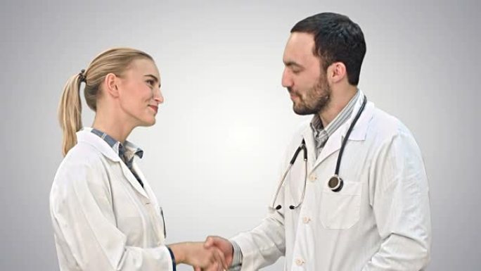 年轻的医生和漂亮的护士在成功的手术后握手，看着白色的背景上的相机