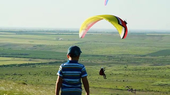 男孩走过滑翔伞翱翔的草原