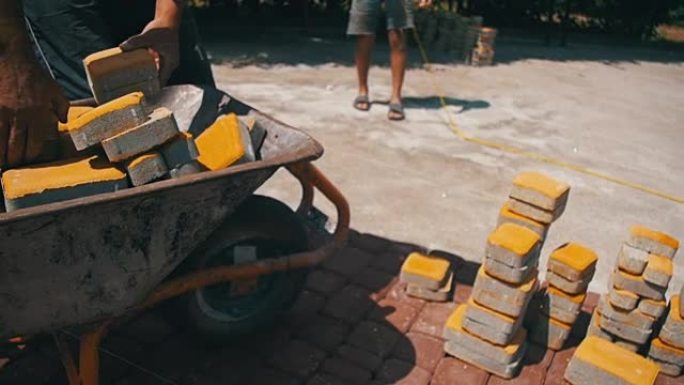 在建筑工地，建筑工人从独轮车上卸下石头铺路。慢动作