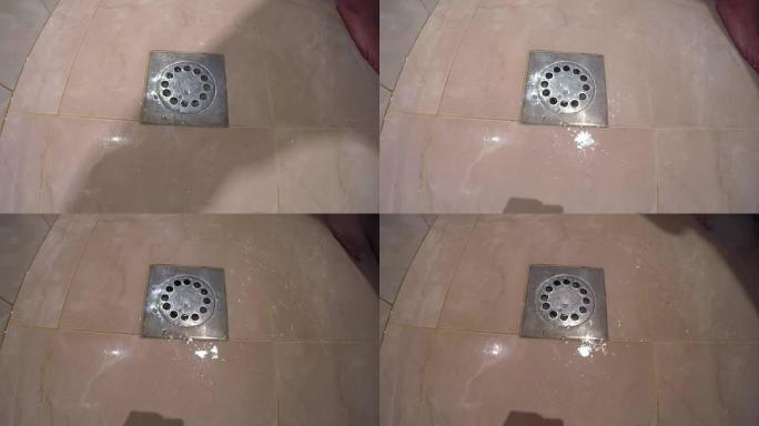 男子在浴室的水中淋浴，从淋浴器排入瓷砖地板上的排水孔
