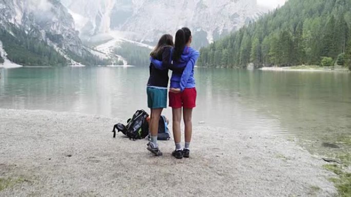 两个女人在布雷斯湖拥抱并谈论风景。一群朋友夏季户外探险之旅。探索意大利多洛米蒂阿尔卑斯山的旅行。4k