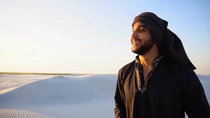 在晴朗温暖的夜晚，自信英俊的阿拉伯男子在坎杜尔行走在白色的沙漠中间
