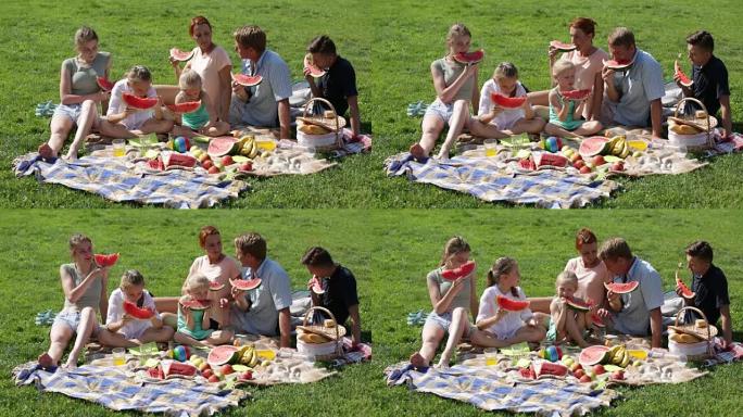 有四个孩子的男人和女人在野餐时吃西瓜