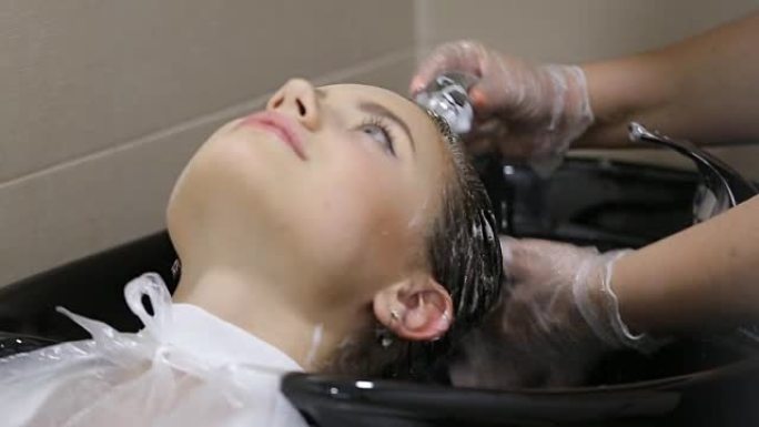 穿着手套的理发师在沙龙洗年轻女子的头发
