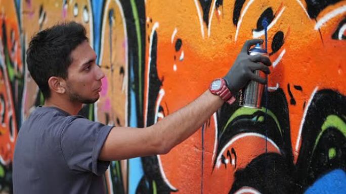 街头艺术家在普通的墙上画彩色涂鸦-现代艺术概念与城市人表演和准备活壁画与喷雾剂颜色喷雾-阳光明媚的下