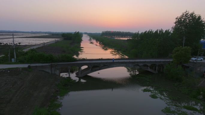 女生站在乡村小桥上在夕阳落日下挥手