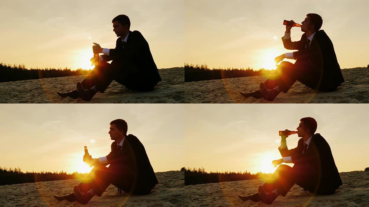 一个穿着西装的年轻人坐在沙滩上，从瓶子里喝啤酒。概念-挫折、破产、抑郁