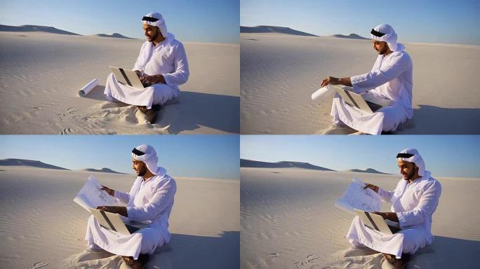 在炎热的夏天，阿拉伯阿拉伯的阿拉伯酋长建筑师坐在沙漠的沙子上，手提电脑