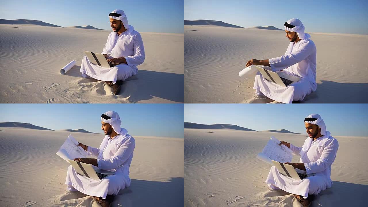 在炎热的夏天，阿拉伯阿拉伯的阿拉伯酋长建筑师坐在沙漠的沙子上，手提电脑