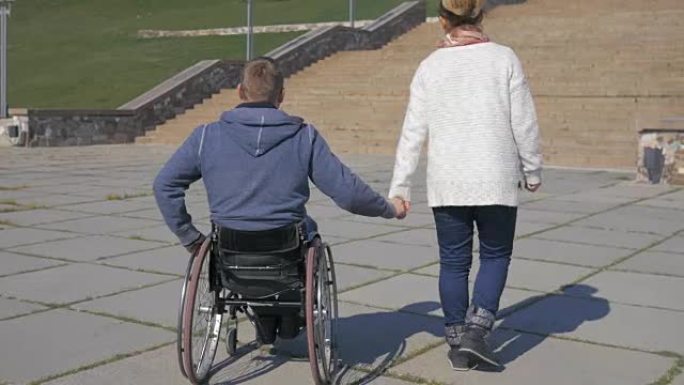 情侣，轮椅上的残疾人和女友在公园散步
