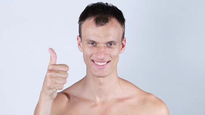 微笑的年轻裸胸男子的肖像与拇指向上
