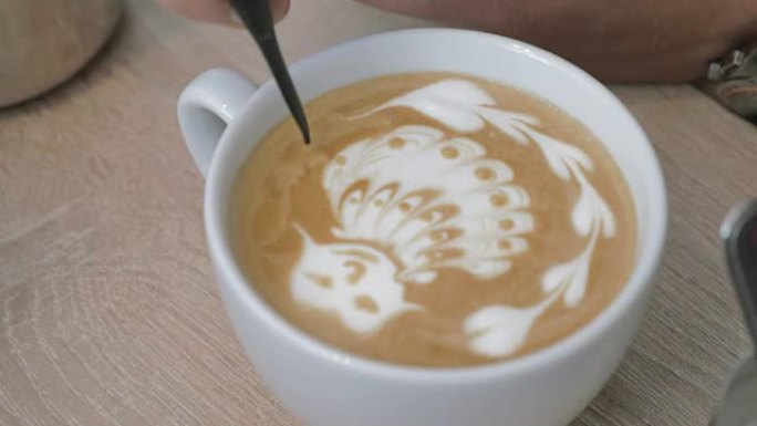 桌子上是一杯带泡沫的咖啡，男人在泡沫图案上画画