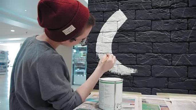 年轻女画家在咖啡店的黑砖墙上做白色设计