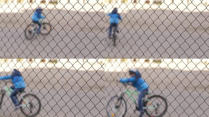 一个穿着运动夹克和黑色眼镜的男孩在网格后面的自行车上