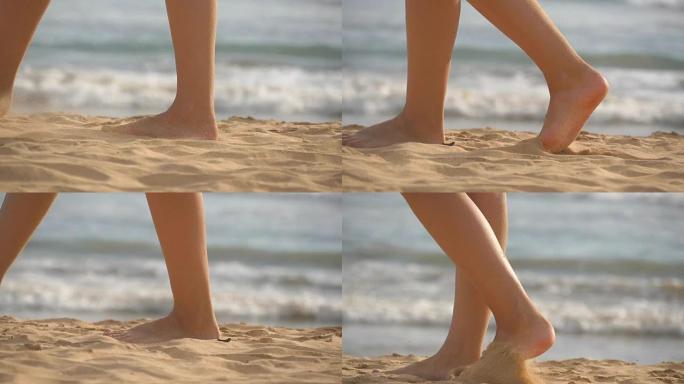 女性的脚在海滩上金色的沙滩上行走，背景是海浪。年轻女子踩在沙滩上的腿。海边的赤脚女孩。暑假假期。慢动