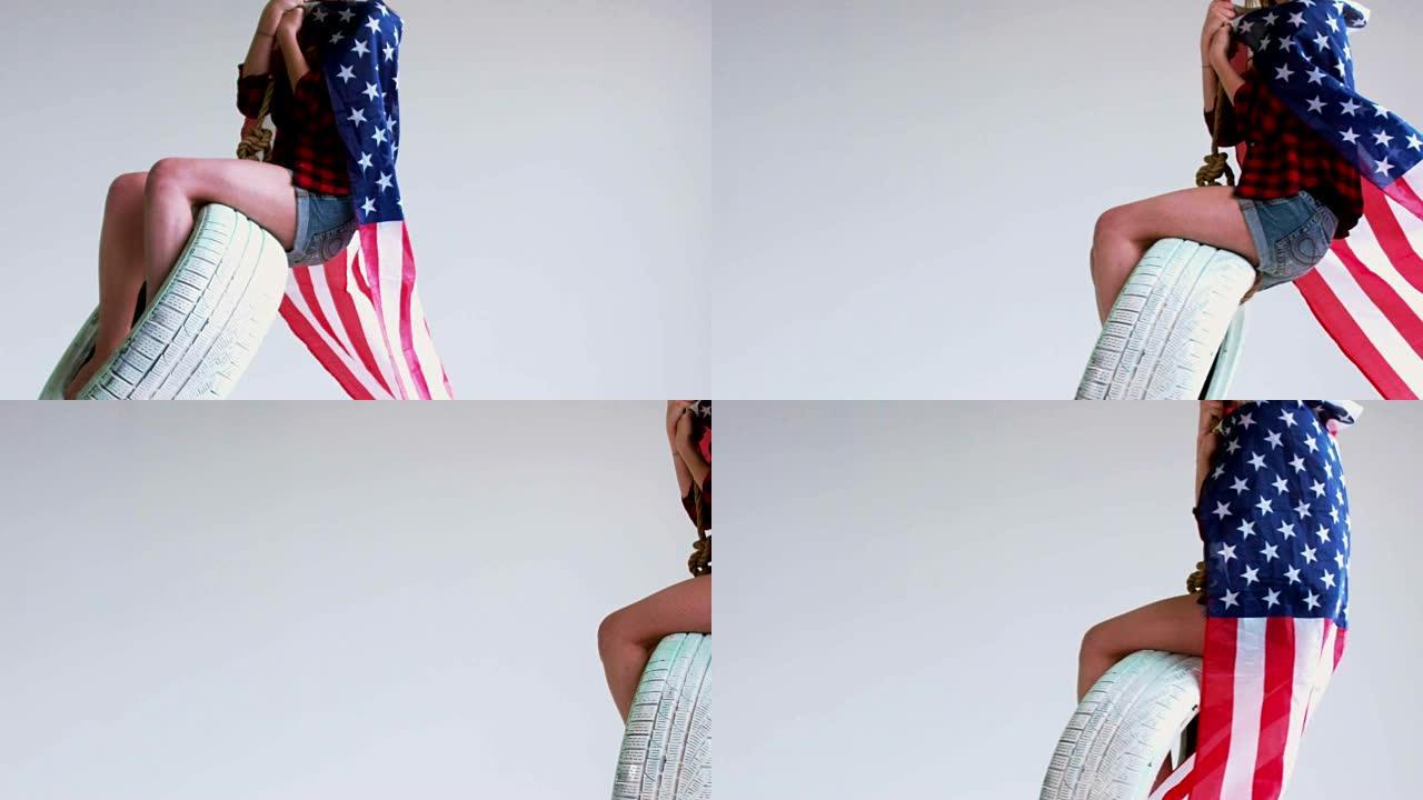 中等镜头的年轻白人女孩与挥舞美国国旗骑在一个轮胎秋千对白色的背景