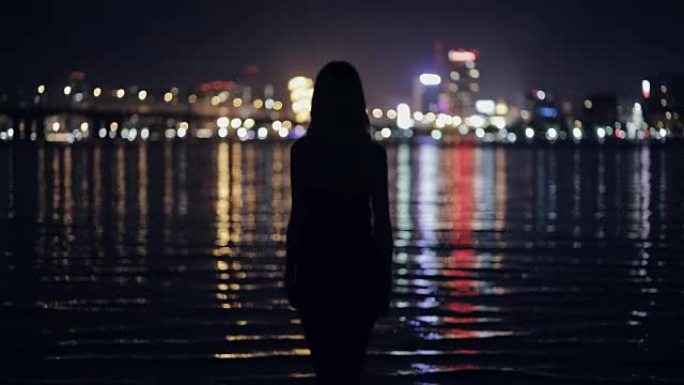 女人看着夜晚的城市景观站在河边