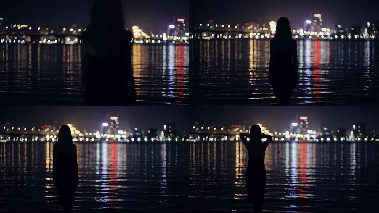 女人看着夜晚的城市景观站在河边