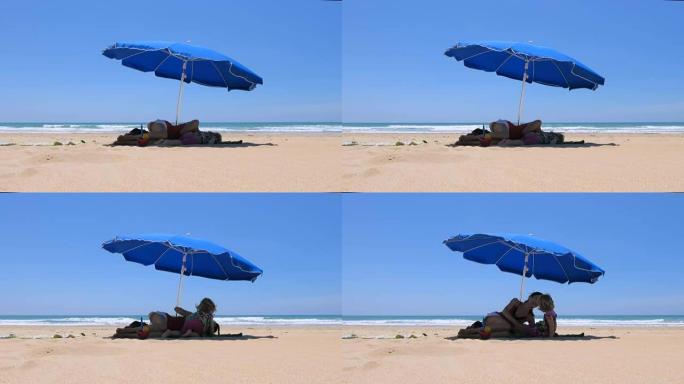 婴儿和母亲躺在海滩上的蓝色阳伞上