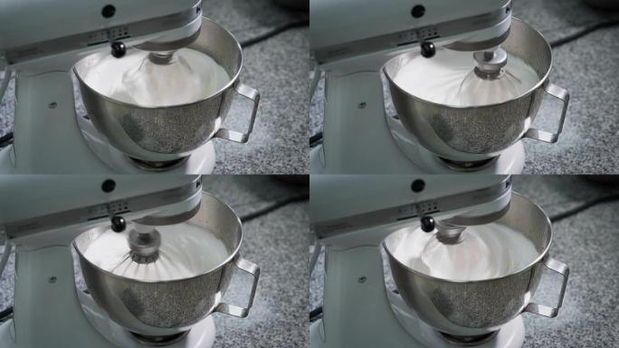在面包店厨房的金属碗中混合奶油和蛋清。糖果制备的专业设备。花冠快速转动