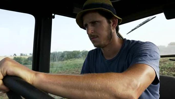 农夫戴着帽子，坐在拖拉机舱里，用犁骑在田野上。