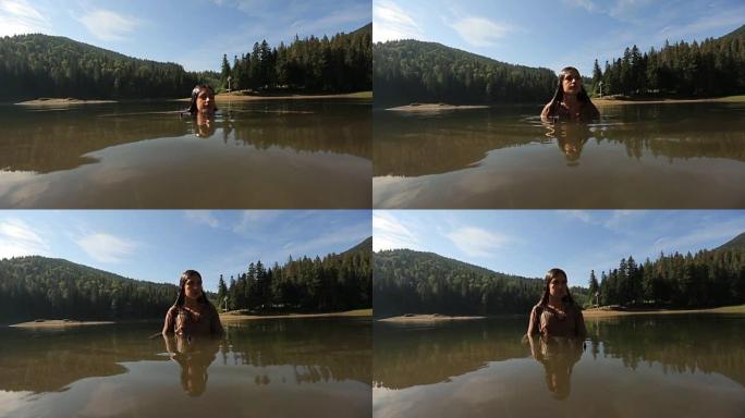 穿着灰色连衣裙的年轻美丽溺水女子从喀尔巴阡山脉的神秘山湖的绿水中慢慢浮出水面