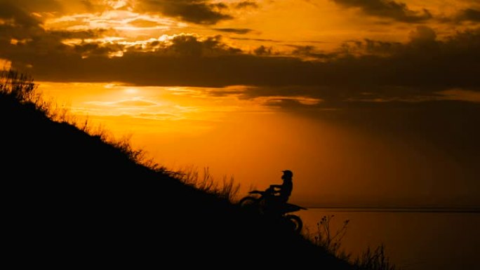 越野摩托车手冲破障碍。爬上马路上的小山。夕阳映红了天空