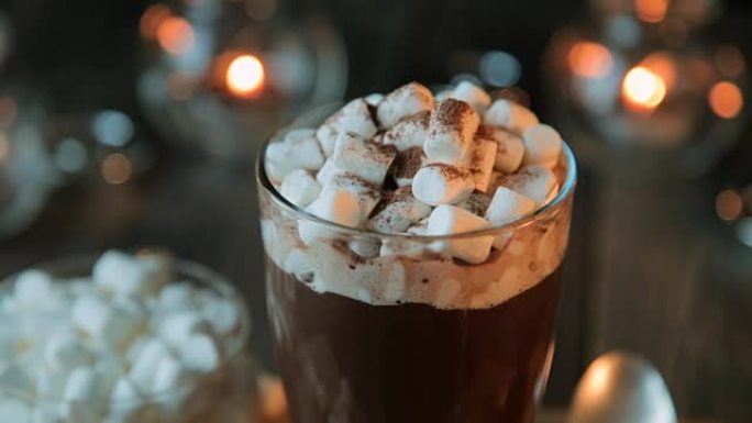 美丽的组成-热巧克力与果酱和巧克力片在一个透明的玻璃。玻璃站在木架上。蜡烛后面在燃烧。特写