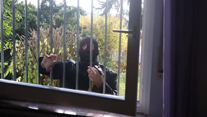 戴面具试图进入有铁栏杆的窗户的窃贼