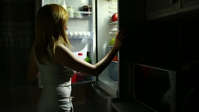 女人晚上打开冰箱。夜间饥饿。饮食。暴食