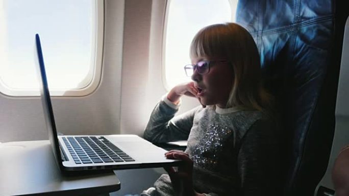 这个女孩6岁坐飞机。有点无聊，想睡觉和打哈欠。在笔记本电脑上看卡通