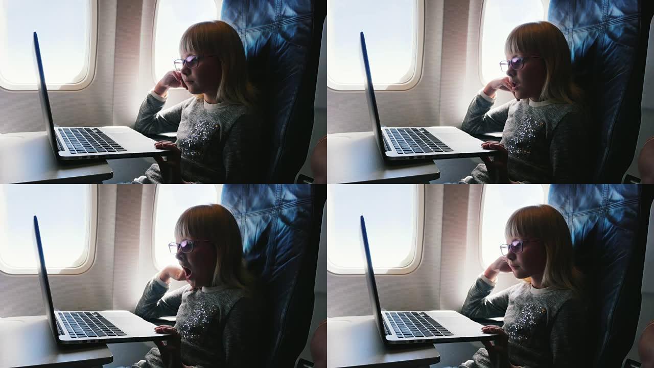 这个女孩6岁坐飞机。有点无聊，想睡觉和打哈欠。在笔记本电脑上看卡通