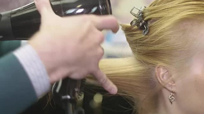 理发师用梳子和吹风机在美容院拉金发女孩的头发。制作体积发型