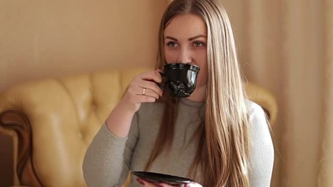 一位迷人的年轻女子的肖像坐在客厅家庭住宅的沙发上，喝着新鲜的咖啡，微笑着。生活的幸福