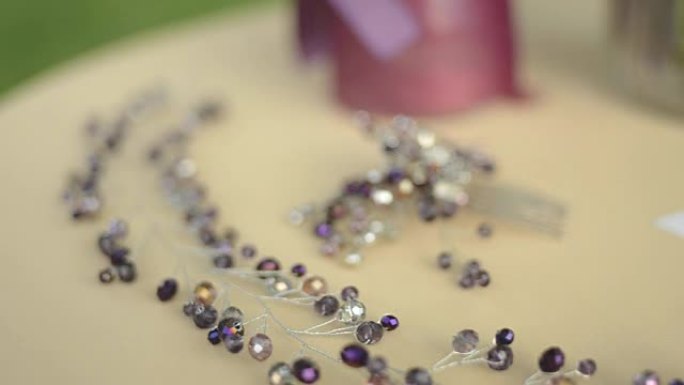桌子上的婚礼配件。紫色花朵，米色织物，胸针或梳子在新娘的头发上。可变焦点，特写。