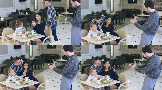 和蔼可亲的服务员在智能手机上给咖啡馆里友好的年轻家庭拍照