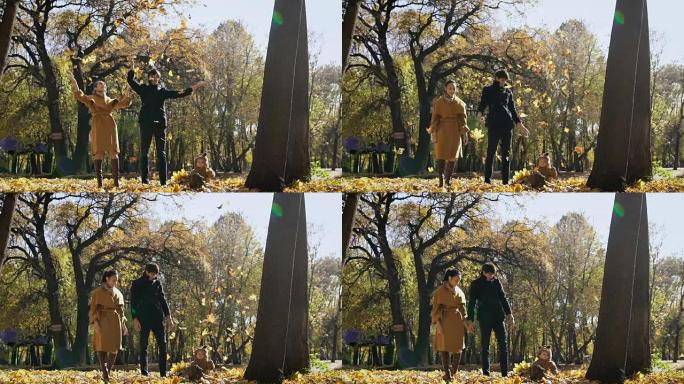 快乐的一家人在公园里玩着秋叶。妈妈和爸爸向空中抛了一圈链子。小孩子看着他们玩得很开心