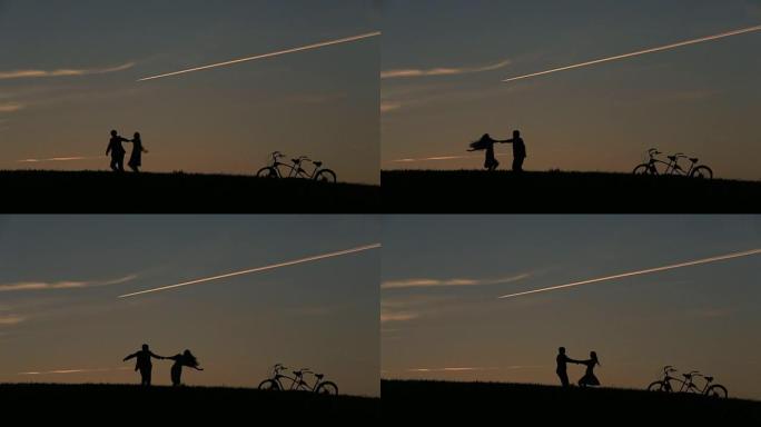 美丽的情侣与双人自行车的剪影在日落时手牵手玩耍