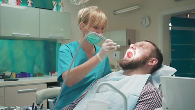 女牙医钻男性患者的牙齿，看着镜头。