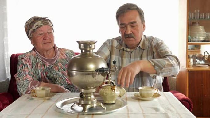 一对老年夫妇用老式的俄罗斯水壶茶壶准备茶。一个留着胡子的男人为妻子倒茶