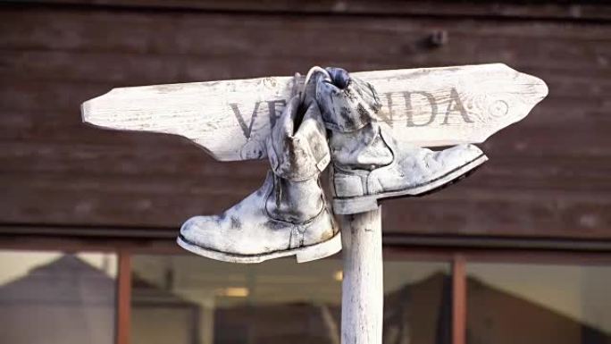 一双旧的白色靴子挂在木制铭牌上，在夏天摆动