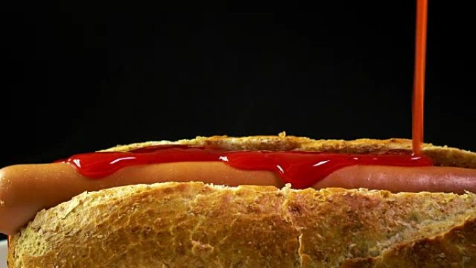 在黑色背景下将番茄酱倒在新鲜制作的热狗上。全球流行的快餐。全高清特写多莉镜头
