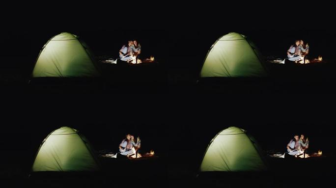 年轻夫妇在篝火和帐篷周围的木棍上烤棉花糖