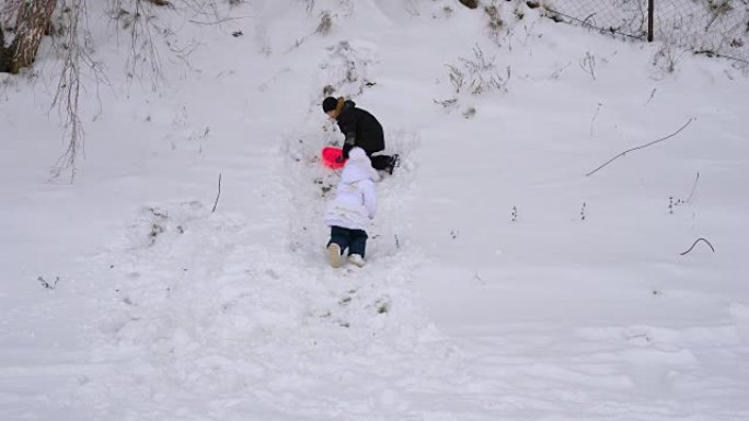 孩子们正试图在山坡上骑行。男孩和女孩滚下山坡。公园里孩子们的冬季乐趣。阴天的冬日。