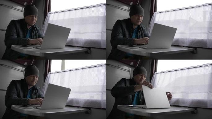 火车上的一个年轻人，在笔记本电脑上打印，微笑着，放下笔记本电脑的盖子，直视他的面前