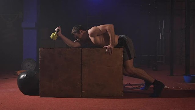 性感的赤裸上身的男人在箱子上做二头肌运动，获得很大的力量，像机车一样喘着气
