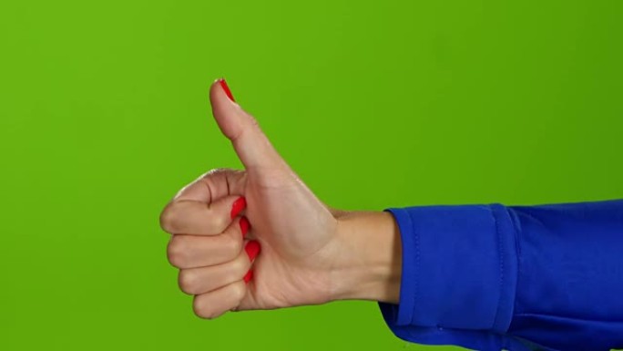 在绿色屏幕背景上竖起大拇指的手。手语